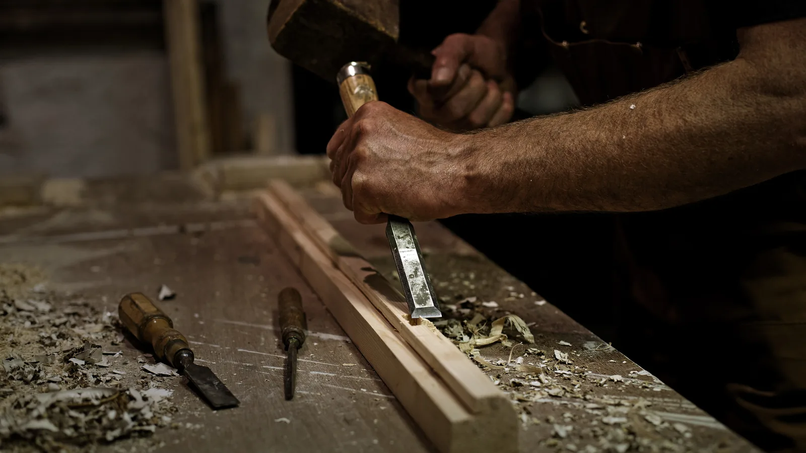 An LTM joiner cutting a moulding by hand with a chisel at the bench