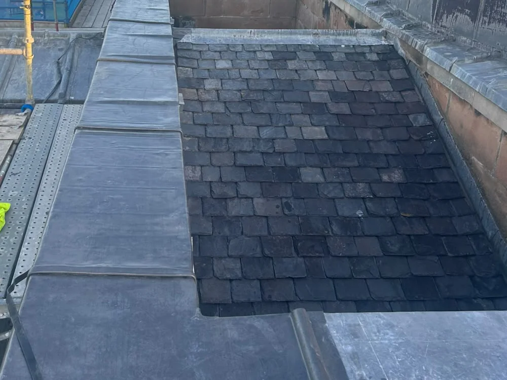 A parapet cope covered in sheet lead, bay by bay with lapped joints, beside a newly slated roof