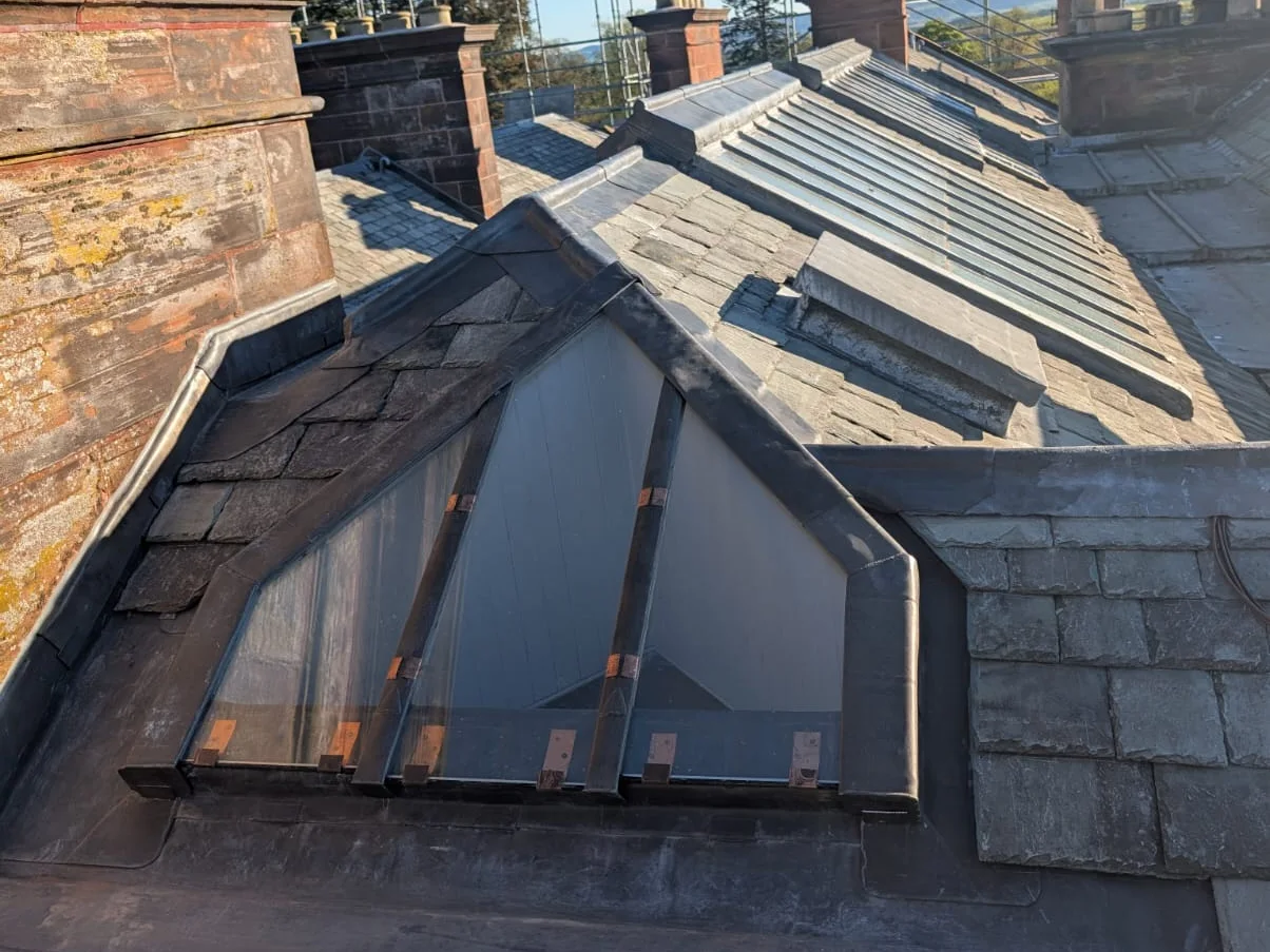 A gabled rooflight framed in lead: glazing bars capped, glass held on copper tingles, and a lead apron across the foot