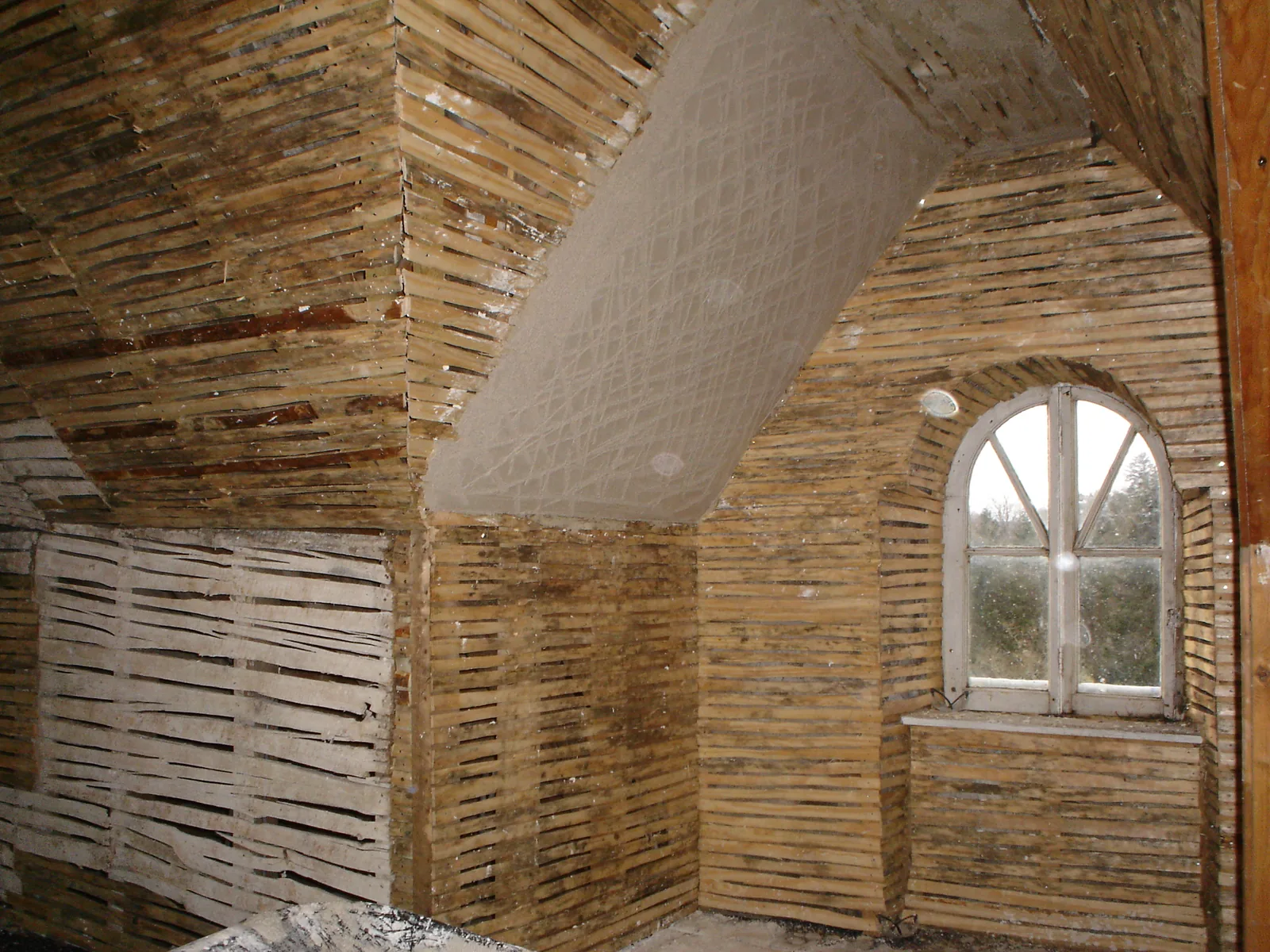 An attic room fully lathed for lime plaster, the new laths following the coombed ceiling and the arched window