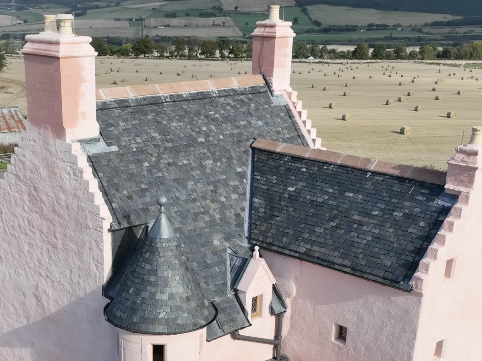 A harled tower house re-slated in Scotch slate: the main roof, the wing and the conical turret roofs, with the chimney heads and skews renewed