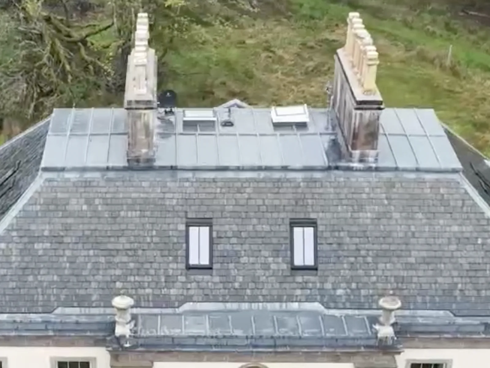 A piended slate roof re-laid in diminishing courses, with lead-dressed platform, ridges and dormers between the urn finials