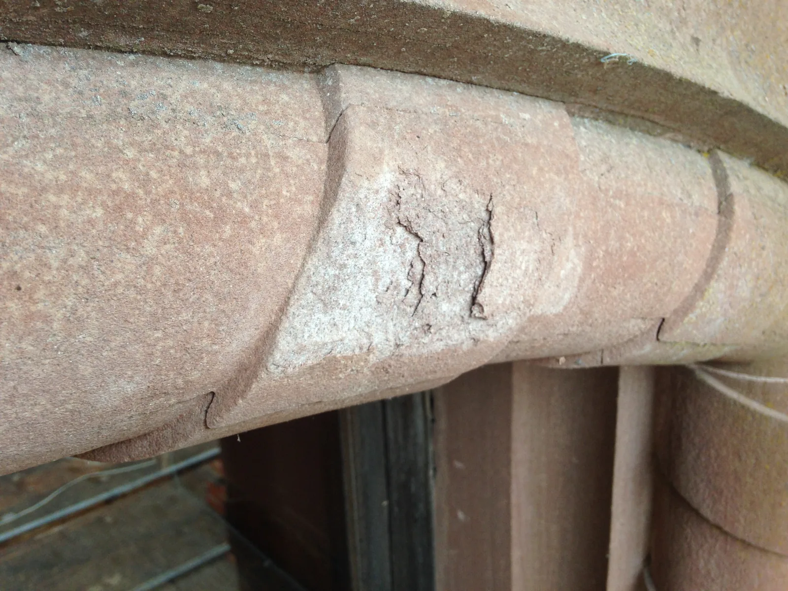 A red sandstone door surround with the moulded arch cracked and delaminating