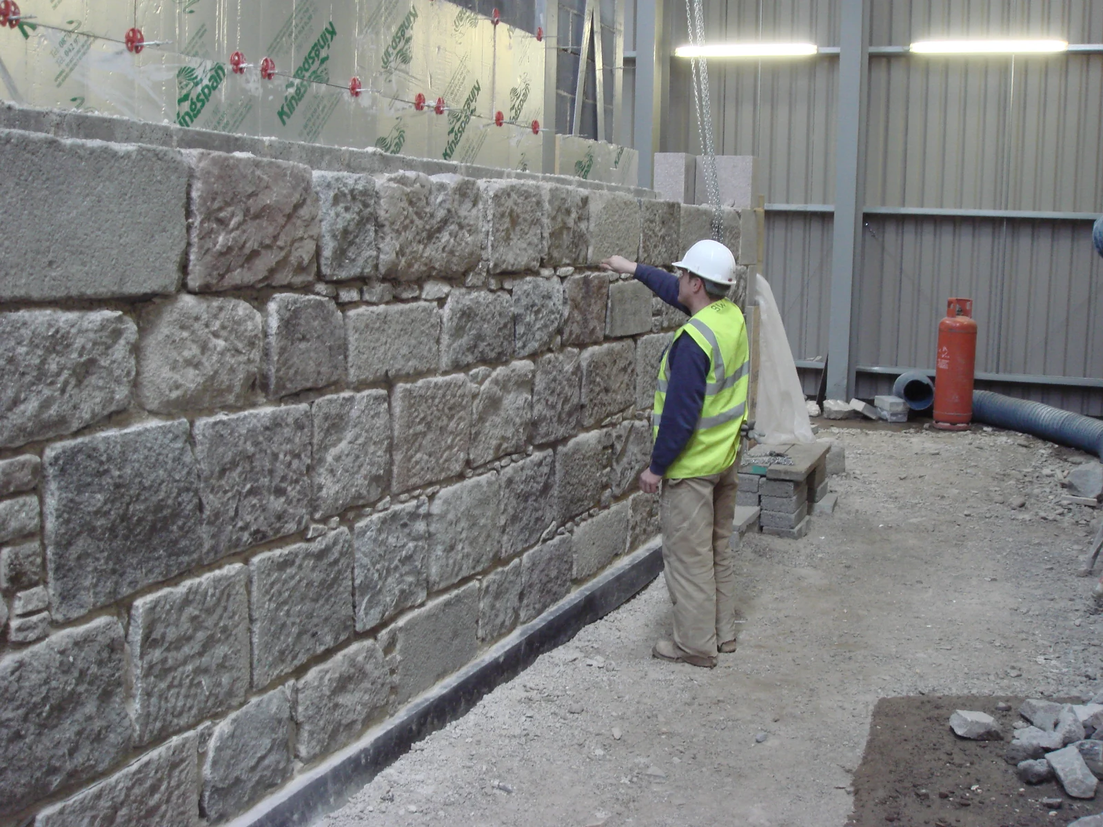 Ben Alder Chapel: the reclaimed squared granite outer leaf built in hot lime inside the heated enclosure that let lime work continue through a Highland winter